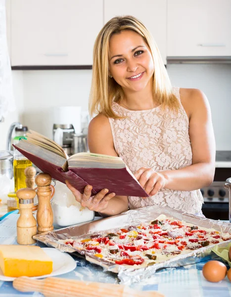 Mulher com livro de receitas cozinhar pizza — Fotografia de Stock