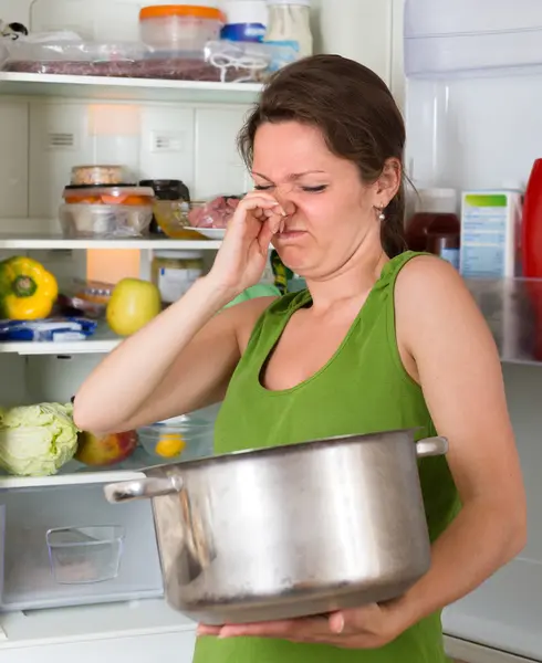 Mujer sosteniendo comida asquerosa cerca de la nevera — Foto de Stock