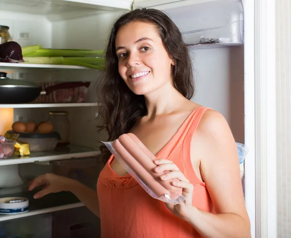 Девушка берет сосиски из холодильника — стоковое фото