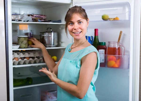 Mujer sonriente cerca de la nevera llena — Foto de Stock