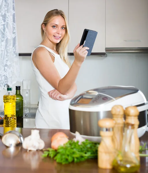 Vrouw lezing ereader in de buurt van multicooker — Stockfoto