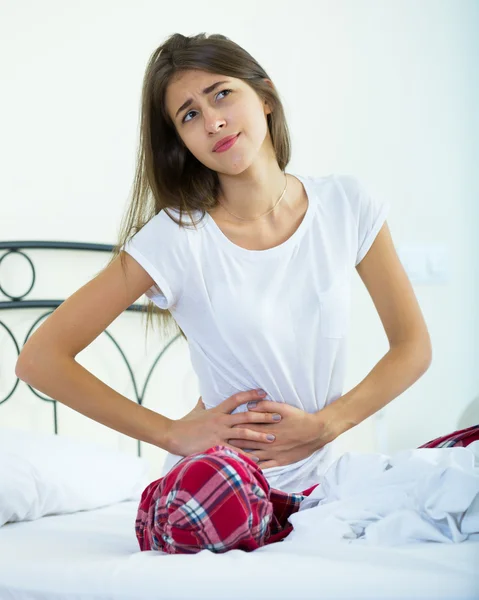 Portrait of brunette girl in bed with stomach pain — Stock Photo, Image