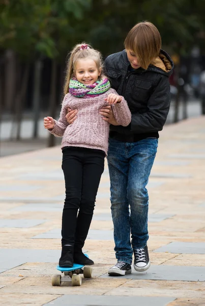 Brother learning sister to ride skateboard — Stock Photo, Image