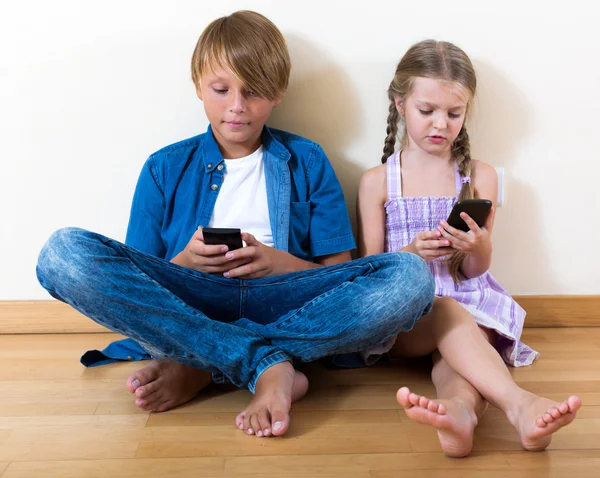 Irmãos positivos brincando com telefones — Fotografia de Stock