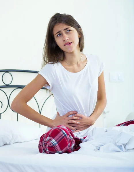 Brunette girl in bed with stomach pain — Stock Photo, Image