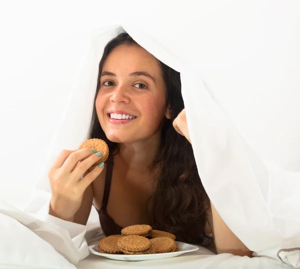 Kvinna äta kakor i sängen — Stockfoto