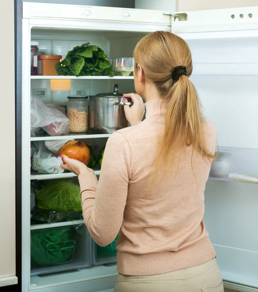 Довольная домохозяйка рядом с заполненным холодильником — стоковое фото