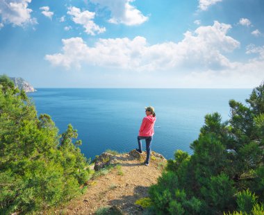 Tepenin tepesinde duran ve körfezdeki sakin denizi izleyen bir kız. Seyahat ve doğa sahnesindeki insanlar.