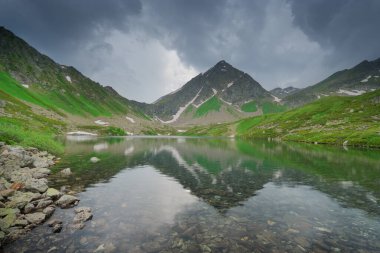 Göl kenarındaki berrak dağ yansıması üzerinde sağanak yağmurlu bulutlar. Doğa manzarası.