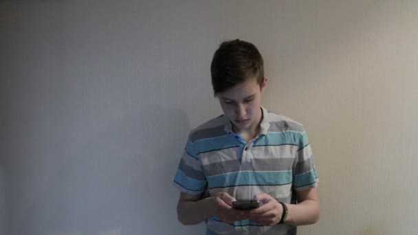 Adolescente chico mensajes de texto usando aplicación en el teléfono inteligente en la noche cerca de la pared — Vídeos de Stock