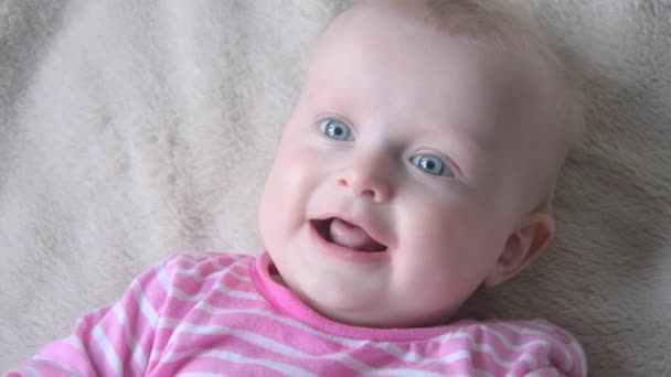 Cute little baby is looking into the camera and is happy on a bed sheet — Stock Video