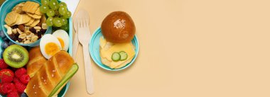 Okul beslenme çantasında turuncu arka planda sandviç, sebze ve meyve var. Üst görünüm, alanı kopyala