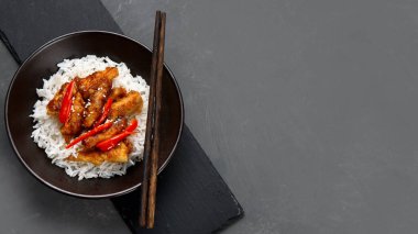 Sos içinde pişirilmiş tavuk, gri arka planda pirinç ve sebzelerle servis ediliyor. Üst görünüm, alanı kopyala