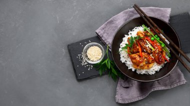 Sos içinde pişirilmiş tavuk, gri arka planda pirinç ve sebzelerle servis ediliyor. Üst görünüm, alanı kopyala