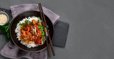 Sos içinde pişirilmiş tavuk, gri arka planda pirinç ve sebzelerle servis ediliyor. Üst görünüm, alanı kopyala