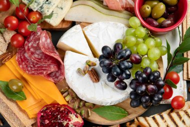 Aperatif masası. Koyu arka planda peynir, fuit ve et panosu. Üst görünüm, 