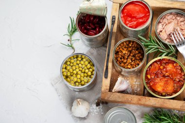 Çeşitli konserve sebzeler, alüminyum kutularda balık ve bezelye. Açık gri arka planda. Üst görünüm, alanı kopyala