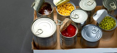 Fasulye, bezelye, mısır, karton kutuda domates gibi konserve sebzeler. Teneke kutular. Karanlık arka plan. Boşluğu kopyala, panorama pankartı