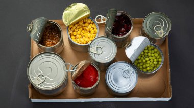 Fasulye, bezelye, mısır, karton kutuda domates gibi konserve sebzeler. Teneke kutular. Karanlık arka plan. Üst Manzara, Panorama Banne