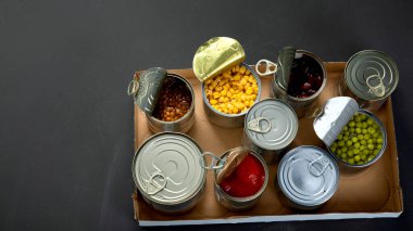 Fasulye, bezelye, mısır, karton kutuda domates gibi konserve sebzeler. Teneke kutular. Karanlık arka plan. Üst görünüm, Spac kopyala