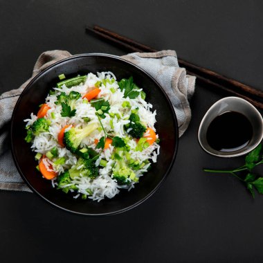 Taze ve sağlıklı vegan pirinç kasesi brokoli, havuç ve yanında çubuklarla taze soğan ile servis edilir. Karanlık arka plan. Üst görünüm