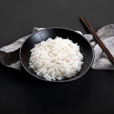 Yanında soya sosu ve yemek çubuğu olan siyah kâsede kaynamış Asya usulü pirinç. Koyu arkaplan