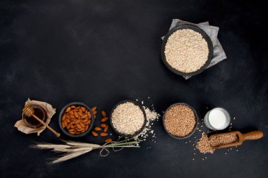 Siyah kaselerde yuvarlanmış yulaf ezmesi ve koyu arkaplanda altın buğday kulakları. Üst görünüm, alanı kopyala