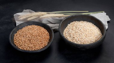 Siyah kaselerde yuvarlanmış yulaf ezmesi ve arka planda altın buğday kulakları.. 