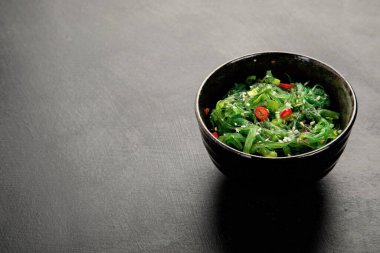 Gri arka planda susamlı ve biberli Wakame yosunu. Asya yemekleri konsepti. Üst görünüm, alanı kopyala