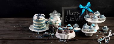 Delicious cake and cupcakes in blue on wooden background. Table setting for celebration. Chalkboard, panoram