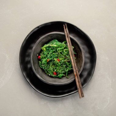 Gri arka planda susamlı ve biberli Wakame yosunu. Asya yemekleri konsepti. Üst görünüm