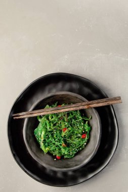 Gri arka planda susamlı ve biberli Wakame yosunu. Asya yemekleri konsepti. Üst görünüm, alanı kopyala