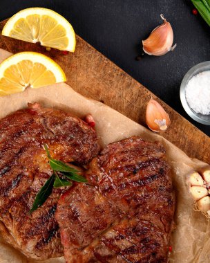 Delicious prepared meat steaks with seasoning and herbs on dark background. Geilled food concept. Top view, copy space