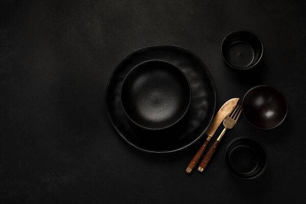 Table setting with a black plates on a black background. Minimalism concept. Top view, copy space