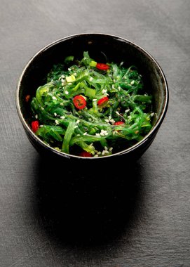 Gri arka planda susamlı ve biberli Wakame yosunu. Asya gıda kavramı. 