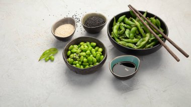 Raw edamame soya beans with salt and sauce on light gray background.  clipart