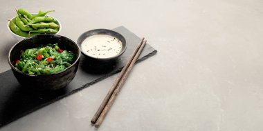 Gri arka planda susamlı ve biberli Wakame yosunu. Asya yemekleri konsepti. Boşluğu kopyala