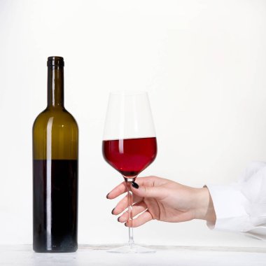 Beyaz arka planda bir bardak gül şarabı tutan genç bir kadın. Siyah ojeli el..