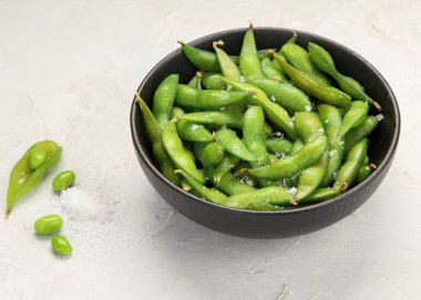 Çiğ edamame soya fasulyesi açık gri arka planda tuz ve sos ile. 