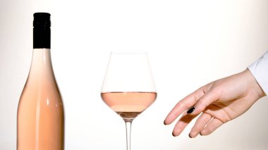 Beyaz arka planda bir bardak gül şarabı tutan genç bir kadın. Siyah ojeli el..