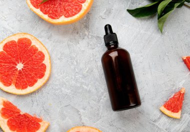 Greyfurtlu bir şişe aroma yağı ve açık gri arka planda yapraklar. Üst görünüm, düz görünüm, kopyalama alanı