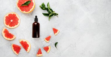 Greyfurtlu bir şişe aroma yağı ve açık gri arka planda yapraklar. Üst görünüm, düz görünüm, kopyalama alanı