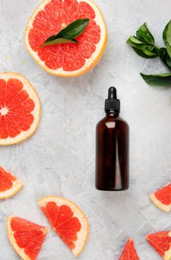 Greyfurtlu bir şişe aroma yağı ve açık gri arka planda yapraklar. Üst manzara, düz uzanma