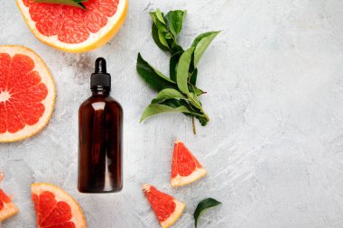 Greyfurtlu bir şişe aroma yağı ve açık gri arka planda yapraklar. Üst görünüm, düz görünüm, kopyalama alanı