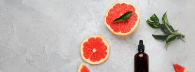 Greyfurtlu bir şişe aroma yağı ve açık gri arka planda yapraklar. Üst görünüm, düz görünüm, kopyalama alanı