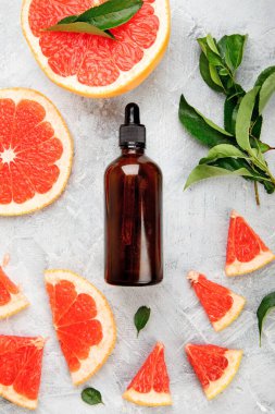 Greyfurtlu bir şişe aroma yağı ve açık gri arka planda yapraklar. Üst görünüm, düz görünüm, kopyalama alanı