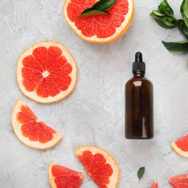 Greyfurtlu bir şişe aroma yağı ve açık gri arka planda yapraklar. Üst manzara, düz uzanma