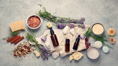 Açık gri arka planda bitkilerle ve çiçeklerle dolu bir şişe gerekli yağ. Üst manzara, düz uzanma