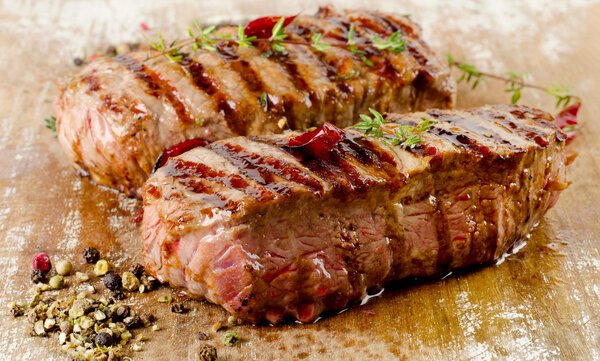 Grilled Beef steaks on a cutting board with herbs