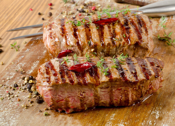 Grilled Beef steaks on a cutting board with herbs